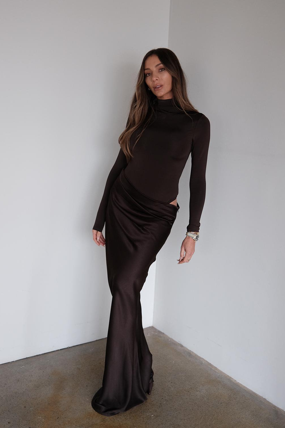 Woman wearing a long black dress standing against a white wall.