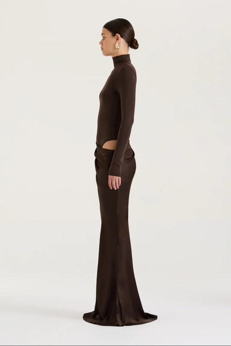 Woman wearing a brown high-neck top and long skirt on a white background